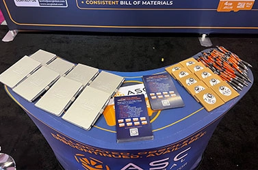 Close-up of the top of ASC Global's booth display at FMS 2026, featuring promotional materials, including product flyers, pens, notebooks, and customer giveaways showcasing the company's industrial memory solutions and supply chain services.